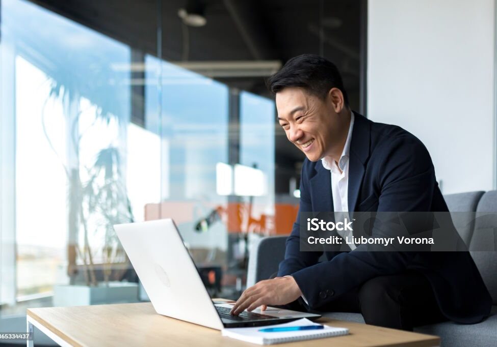 Senior Asian business man working on laptop online, smiling and rejoicing, happy boss business owner working in office