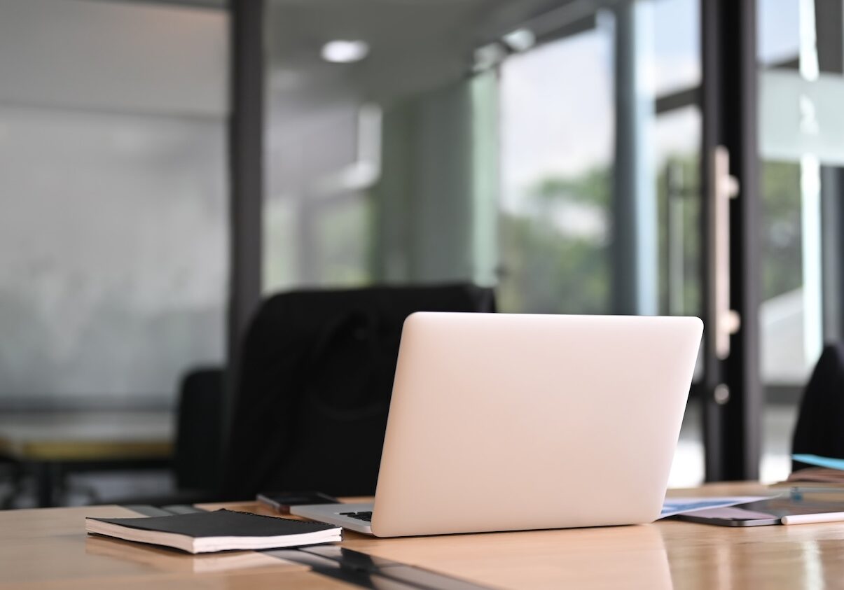 A computer laptop is putting on a meeting table surrounded by various equipment.